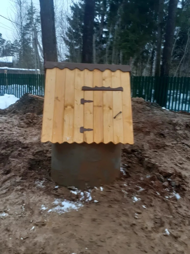 Деревянный домик с двускатной крышей на колодце из бетонных колец